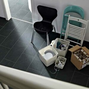 Ein Raum im Umbau, Kartons und Stühle stehen herum. Der Boden ist schwarz gefliest.