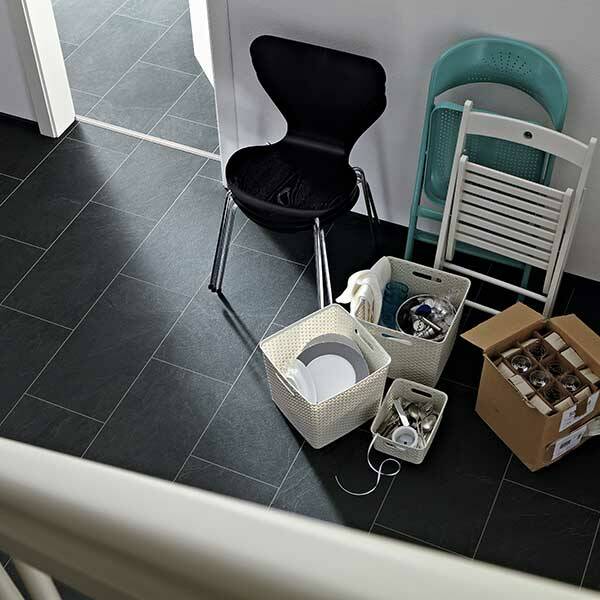 Ein Raum im Umbau, Kartons und Stühle stehen herum. Der Boden ist schwarz gefliest.